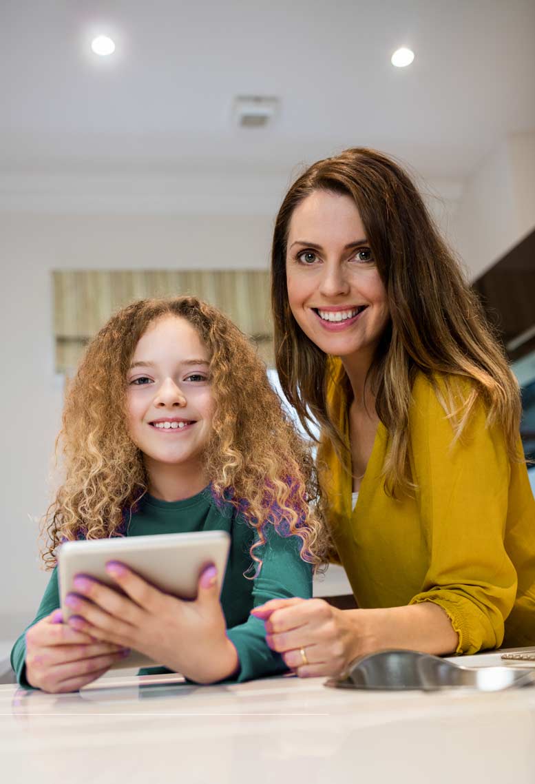 alt="A smiling curly blonde haired kid smiling with her nanny ordering a personalized gift on an iPad"